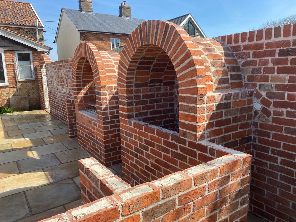 Hand-laid brick arches forming an outdoor kitchen and pizza oven in a Suffolk courtyard