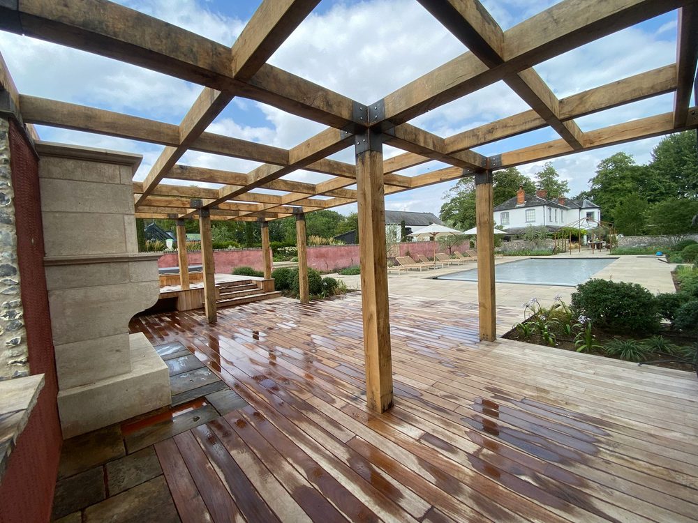 A finished oak pergola over a hardwood deck, looking across the pool — a walled pool garden by Eastscape, Suffolk